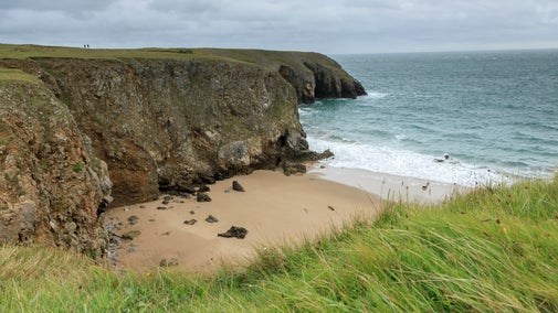 View from cliff top down to small cover with waves and cloudy skies above
